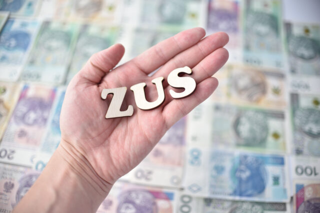 Dlon trzymajaca napis ZUS, w tle poslkie banknoty o roznych nominalach.